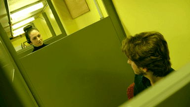 Jone stands over her cubicle barrier, speaking to a colleague